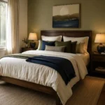 Couple’s bedroom with an olive-green painted wall, navy and olive blankets, cream bedding, dark walnut furniture, warm lamps, and moon artwork