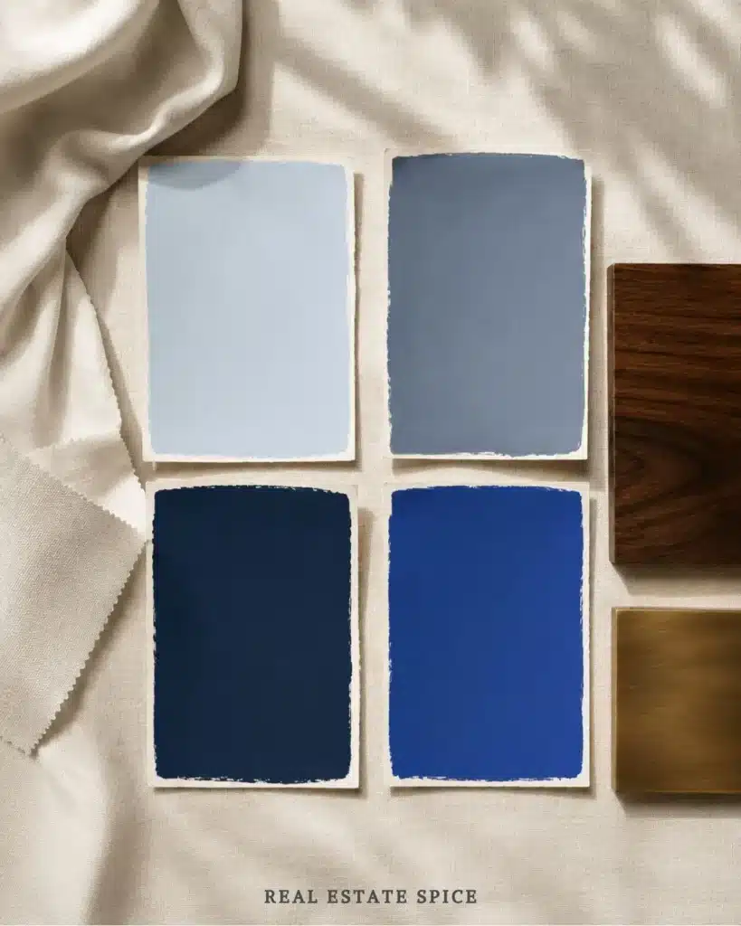 Four blue paint swatches ranging from pale sky blue and smoky blue-gray to deep navy and vivid cobalt beside cream linen, warm wood, and antique brass
