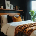 Modern bedroom with a black paneled bed wall, long wood picture ledge, white bedding, and rust-colored accents