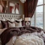 Modern glamorous bedroom with a crystal chandelier, brown accent wall, abstract artwork, tufted bed, and velvet curtains