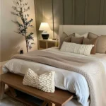 Sage green bedroom with cream bedding, a wood bench, and soft bedside lighting