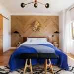 Warm modern bedroom design with a chevron wood accent wall, blue bedding, sliding wood doors, and black light fixtures
