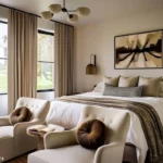 Warm neutral bedroom design for couples with an upholstered bed, bedside sconces, and two cream armchairs