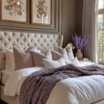 Warm neutral bedroom with cream bedding, taupe walls, rust-orange pillows, and a cozy reading chair