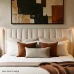 Neutral bed with a channel-tufted headboard, two rust throw pillows, one striped lumbar pillow, and abstract wall art